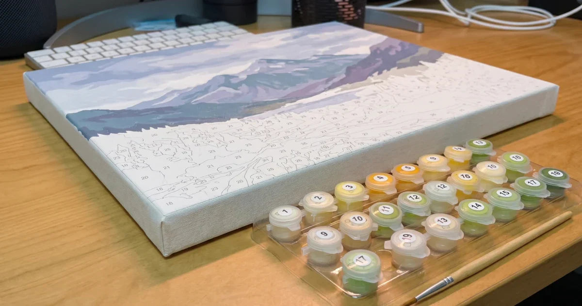 Close-up paint-by-numbers canvas with cotton weave and PKS connected paint pot tray (all closed flip-top lids with white number labels) on a wooden table