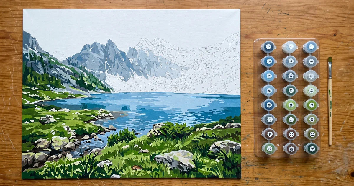 Partially painted paint-by-numbers mountain landscape canvas with PKS connected paint pot tray and brush on a wooden table