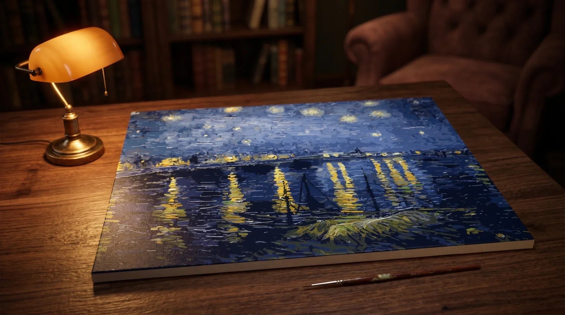 The Starry Night Over the Rhône paint-by-numbers canvas displayed on a wooden table under a brass banker's lamp in cozy evening interior light, with a thin paintbrush resting in front.