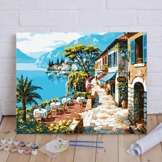 Painting of a scenic Italian town by a lake with a cafe and tables.