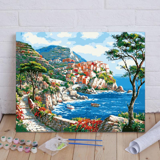 Painting of a coastal village scene on a wooden floor with art supplies.