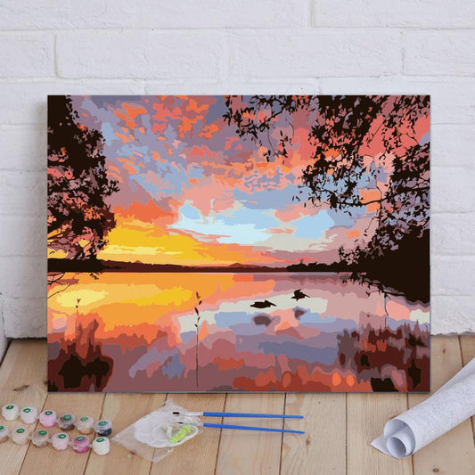 Painting of a sunset over a lake with art supplies on a wooden floor.