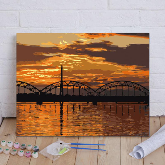 Painting of a sunset over a bridge with art supplies on a wooden floor.