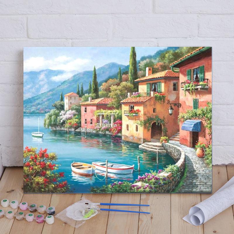 Painting of a scenic Italian village by a lake with boats and flowers on a wooden floor.