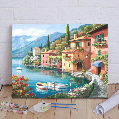 Painting of a scenic Italian village by a lake with boats and flowers on a wooden floor.