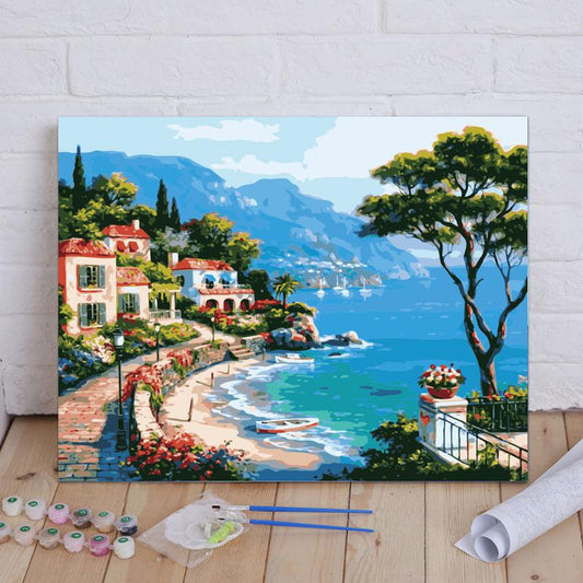 Painting of a coastal scene with houses, trees, and mountains on a wooden floor.