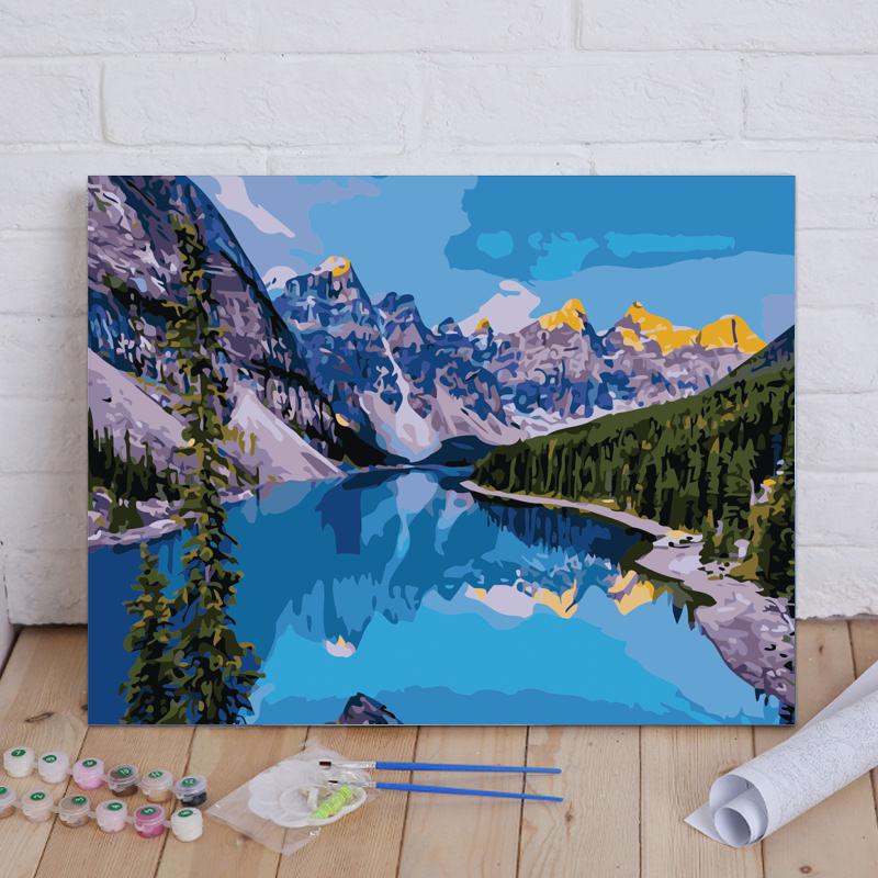 Painting of a mountain lake scene with art supplies on a wooden floor.
