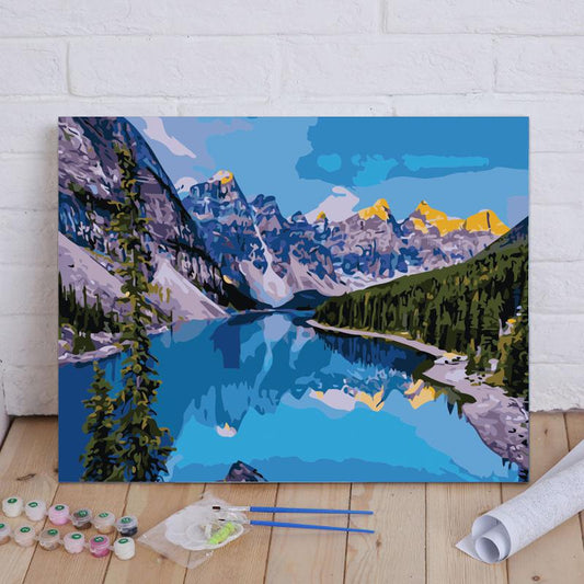 Painting of a mountain lake scene with art supplies on a wooden floor.