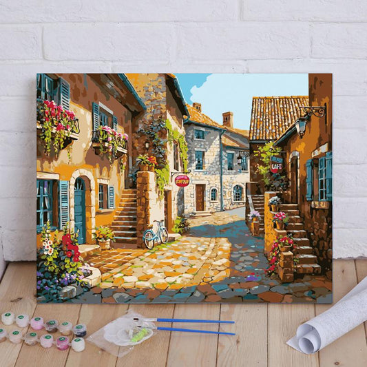 Painting of a quaint European street scene on a wooden floor with art supplies.