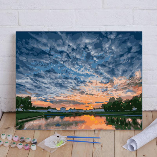 Painting of a sunset over a lake with art supplies on a wooden floor.