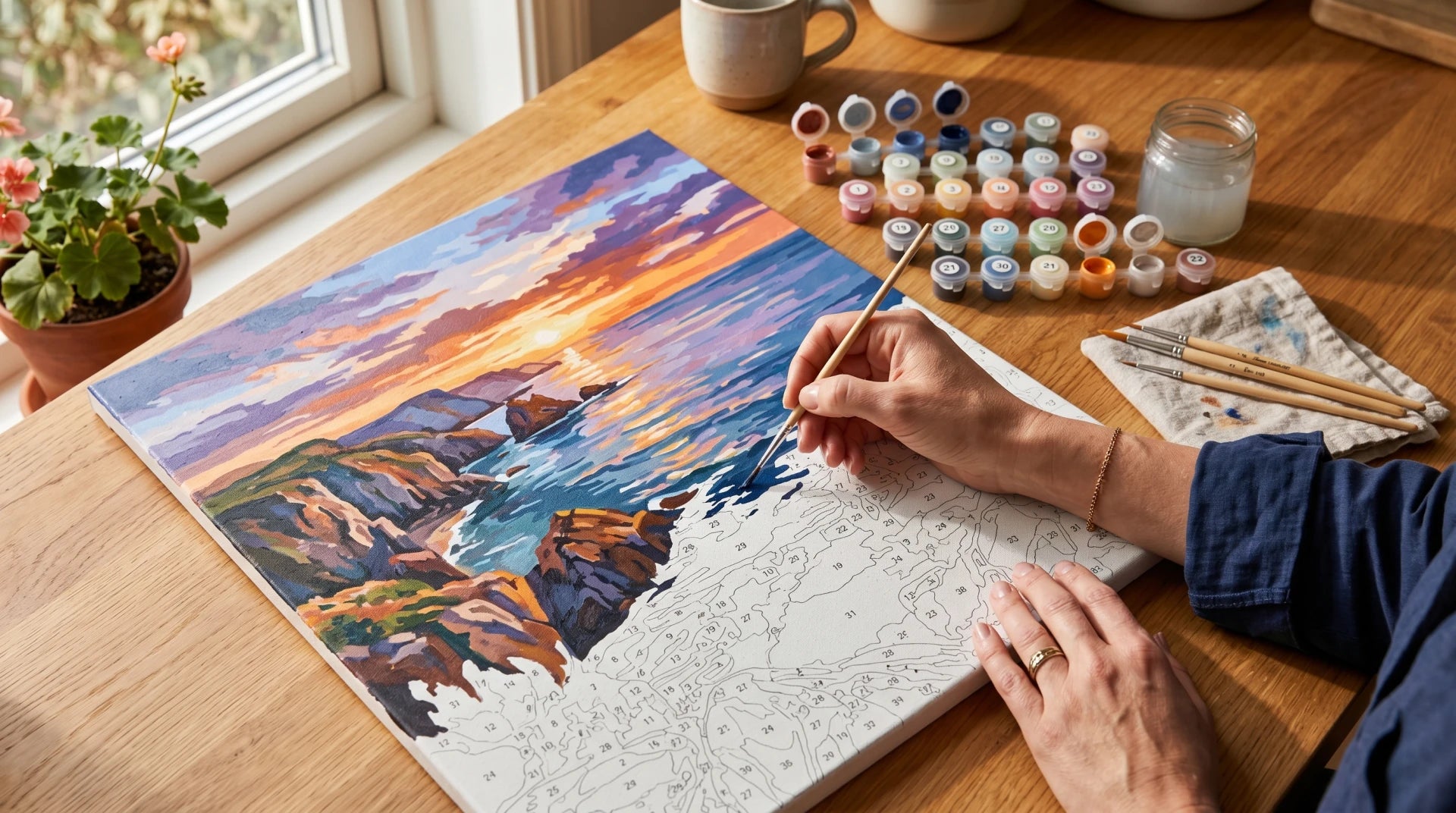 Adult painting a paint-by-numbers coastal scene at a sunlit kitchen table